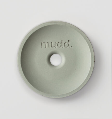 round concrete sample, resembling a puck, in the colour light green with a hole in the centre and the text 'mudd' engraved